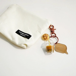 Cute milk tea bear liquid oil keychain accessory for women's bags on a beige canvas pouch