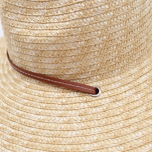 Detail of straw hat texture with brown leather band and silver metal eyelet accent