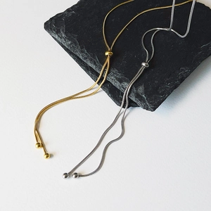Detail of adjustable gold and silver snake bone necklaces on a black stone surface