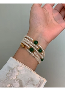 Detail of multi-layer faux pearl bracelet with green beads and gold accents on wrist