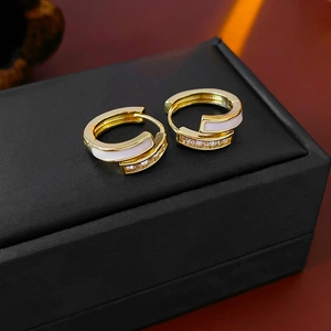 Gros plan de boucles d'oreilles dorées avec émail blanc et zircons étincelants