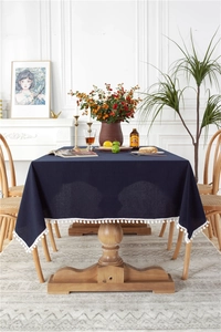 Detail of dark blue cotton tablecloth with white pom-pom fringe on a wooden table