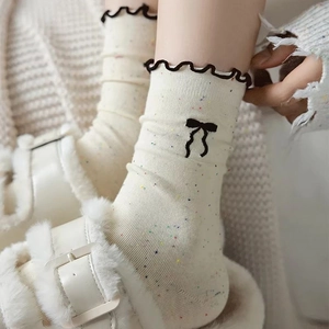 Cream colored crew socks with colorful spots, black ruffle cuffs and a small bow detail