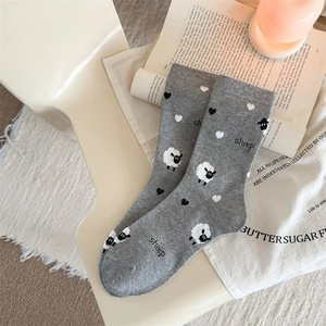 Grey knit crew socks with sheep and heart patterns on a minimalist white chair background
