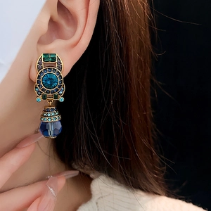 Close-up of vintage gold clip earrings with blue and green crystals on a model