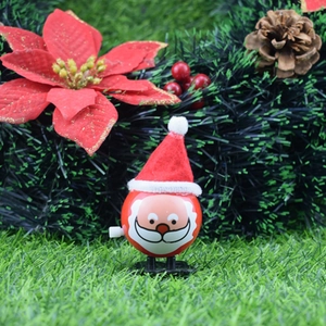 Cute wind-up Santa Claus toy on festive green grass with Christmas wreath background
