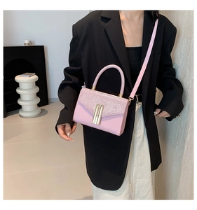 Pink sequin crossbody bag with gold metal bars on the flap held by a model in a studio