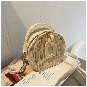 Detail of round straw crossbody bag featuring floral embroidery and adjustable strap