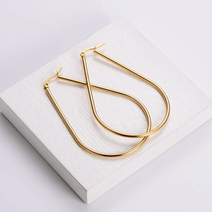 Boucles d'oreilles créoles gouttes en acier titane doré sur un support blanc minimaliste
