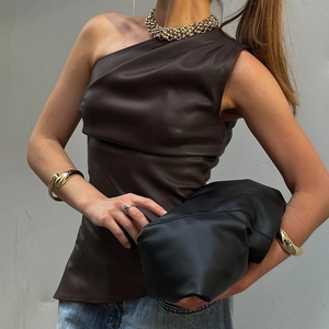 Detail of dark brown one-shoulder faux leather top paired with a gold chain necklace