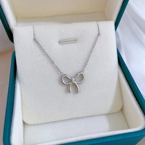 Silver bow pendant necklace in green velvet jewelry box on white fabric background