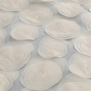 Detailed macro shot of 3D floral appliqués on delicate off-white tulle mesh fabric