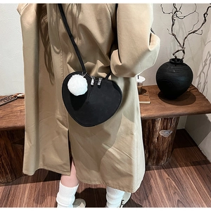 Detail einer mattschwarzen herzförmigen Umhängetasche mit weißem Plüschball-Anhänger