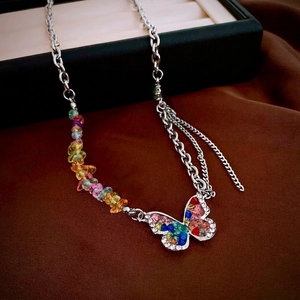 Silver butterfly necklace with colorful stones and layered chains on brown velvet