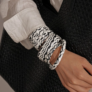 Detail of zebra print resin bangles set on wrist paired with black woven bag