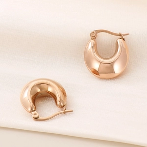 Detailed macro of thick U-shaped rose gold earrings on white silk with a mirror finish