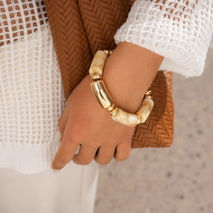 Close-up of Bohemian chunky resin and gold metal bangle on model with woven clutch