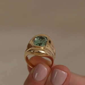 Detail view of a vintage gold ring featuring a square green tourmaline held by a hand