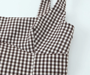 Close-up of brown gingham fabric texture and stitching details on the strap and neckline