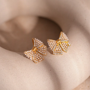 Macro shot of gold bow stud earrings with white faux pearls and zircon on beige background
