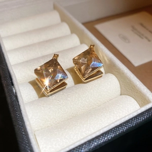 Close-up of champagne crystal diamond-shaped earrings with gold metal base on velvet