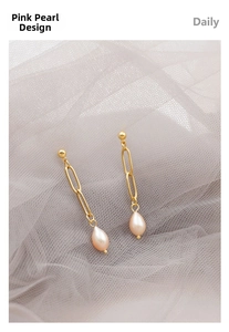 Close-up of gold chain link earrings with elegant pink teardrop pearls on soft mesh