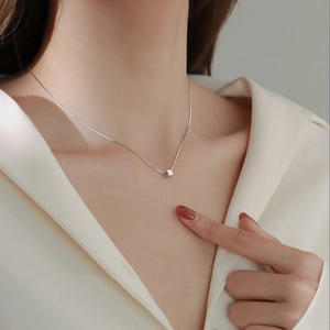 Close-up of a minimalist silver cube pendant necklace worn on a model's neck