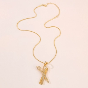 Golden scissors and comb pendant necklace with pavé crystals on a soft pink fabric