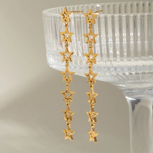 Detailed view of long gold star tassel earrings draped on a textured glass rim