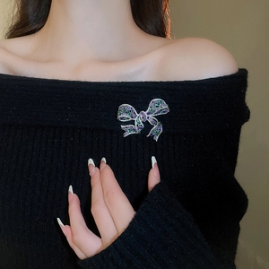 Detailed view of a ribbon bow brooch with purple and green stones on black knitwear