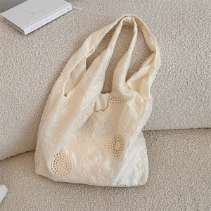 Close-up of intricate floral embroidery and hollow lace detail on a cream canvas tote bag