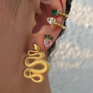 Macro view of gold snake earrings layered with zircon ear cuffs and a pink heart stud
