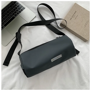 Sac bandoulière cylindrique gris posé à plat sur tissu blanc avec ordinateur et livres