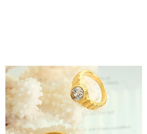 Macro detail of gold textured band ring with round clear stone on white coral