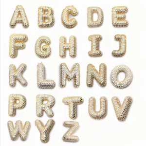 Golden bubble letter pendants set with zircon crystals on a minimalist white background