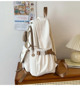 Side view of white canvas backpack with brown straps and side drawstring pocket detail