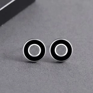 Close-up of minimalist silver hoop earrings with black circular inlay on dark textured background
