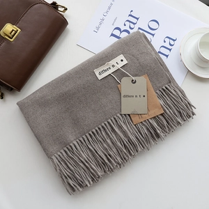 Detailed view of light brown twill scarf with fringe, paper tag and elegant lifestyle setup