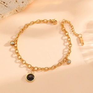 Gold chain bracelet with black stone and sparkling diamond pendants on warm background