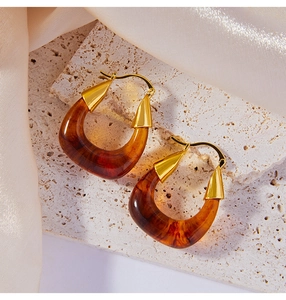 Detailed close-up of U-shaped amber resin and gold-plated copper earrings on stone