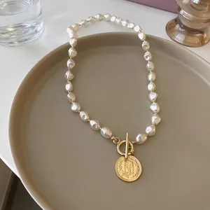 Vintage baroque pearl necklace with golden OT buckle and embossed coin pendant on a tray
