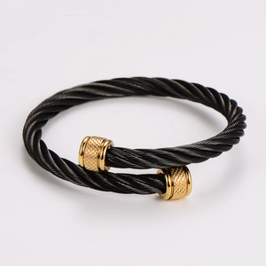 Detail of black cable twist bangle with gold textured cylinder ends on white backdrop