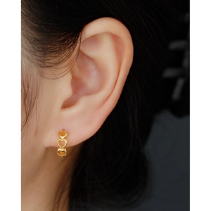 Three linked gold hearts sterling silver huggie earrings worn on model's ear