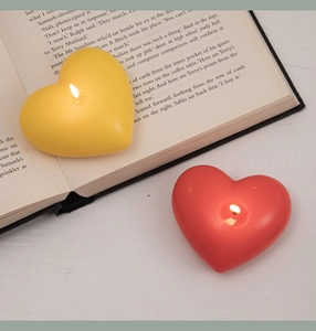 Macro shot of lit red and yellow heart-shaped scented candles on book pages
