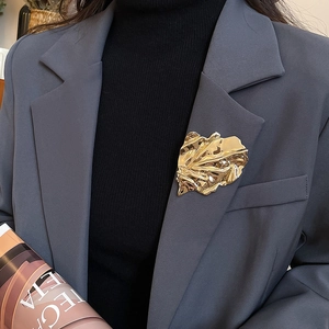 Artistic gold pleated leaf brooch with mirrored finish on dark grey suit lapel