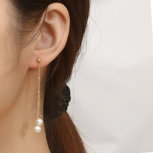 Close-up of elegant gold tassel earrings with dual white pearls on a model