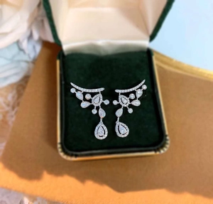 Macro shot of silver drop pear-cut earrings in a premium green velvet jewelry gift box