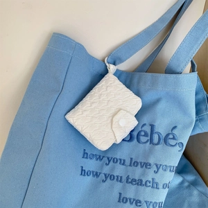Dettaglio della borsa tote in tela blu con mini custodia trapuntata bianca e ricamo