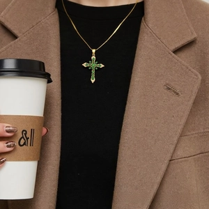 Detail of 18K gold-plated cross necklace with green zircon stones on model outfit