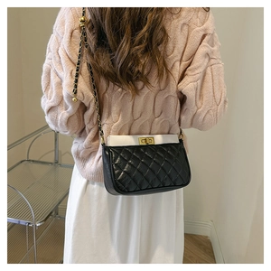 Detail of crossbody bag with black quilted base, white top, and golden chain strap